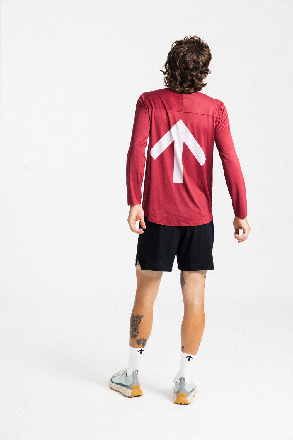 Back view of a male runner wearing the AROW Marathon Short v.2 in Black and Black with a red long sleeve top
