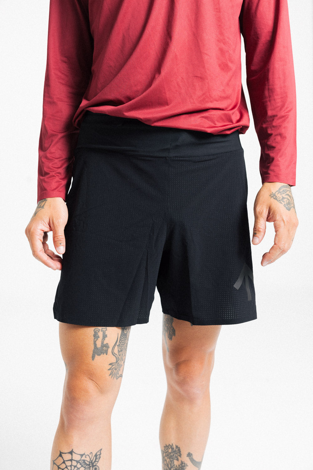 Close-up of the AROW Marathon Short v.2 in Black and Black worn with a red long sleeve top