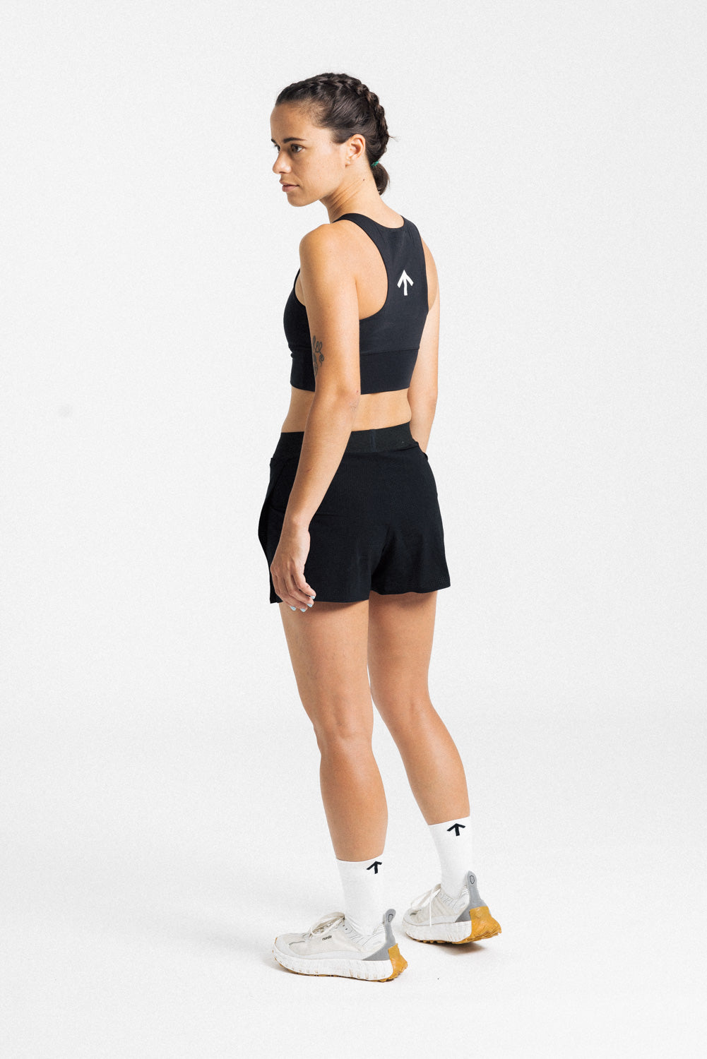 Female runner looking back, showing the white arrow on the back of the AROW Women's Running Bra