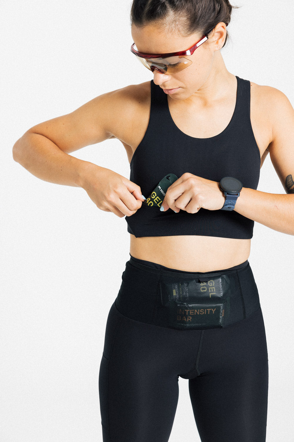 Female runner in sport sunglasses stows a gel in the AROW Women's Running Bra storage waistband.