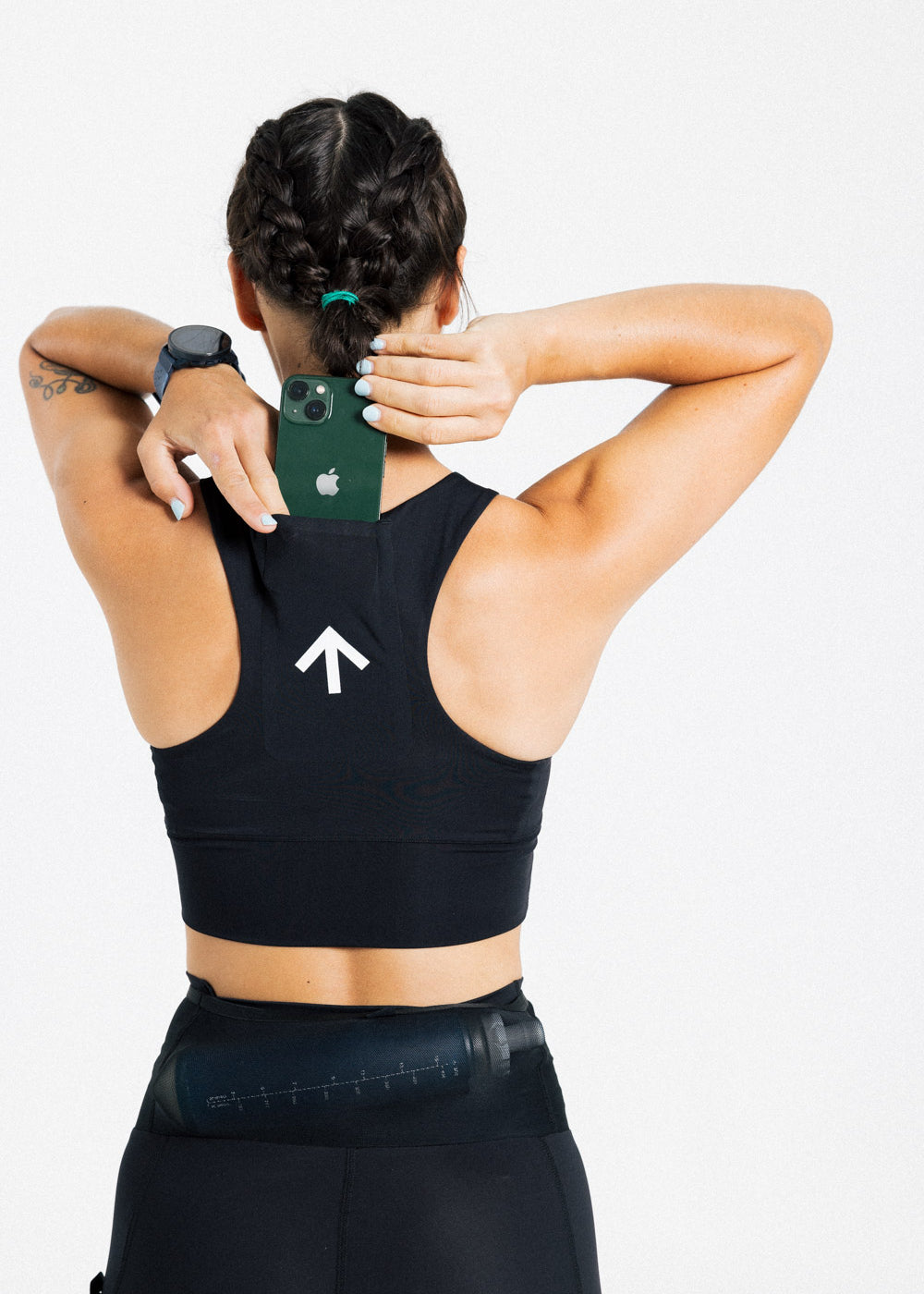 Back view of a female runner storing a phone in the rear pocket of the AROW Women's Running Bra