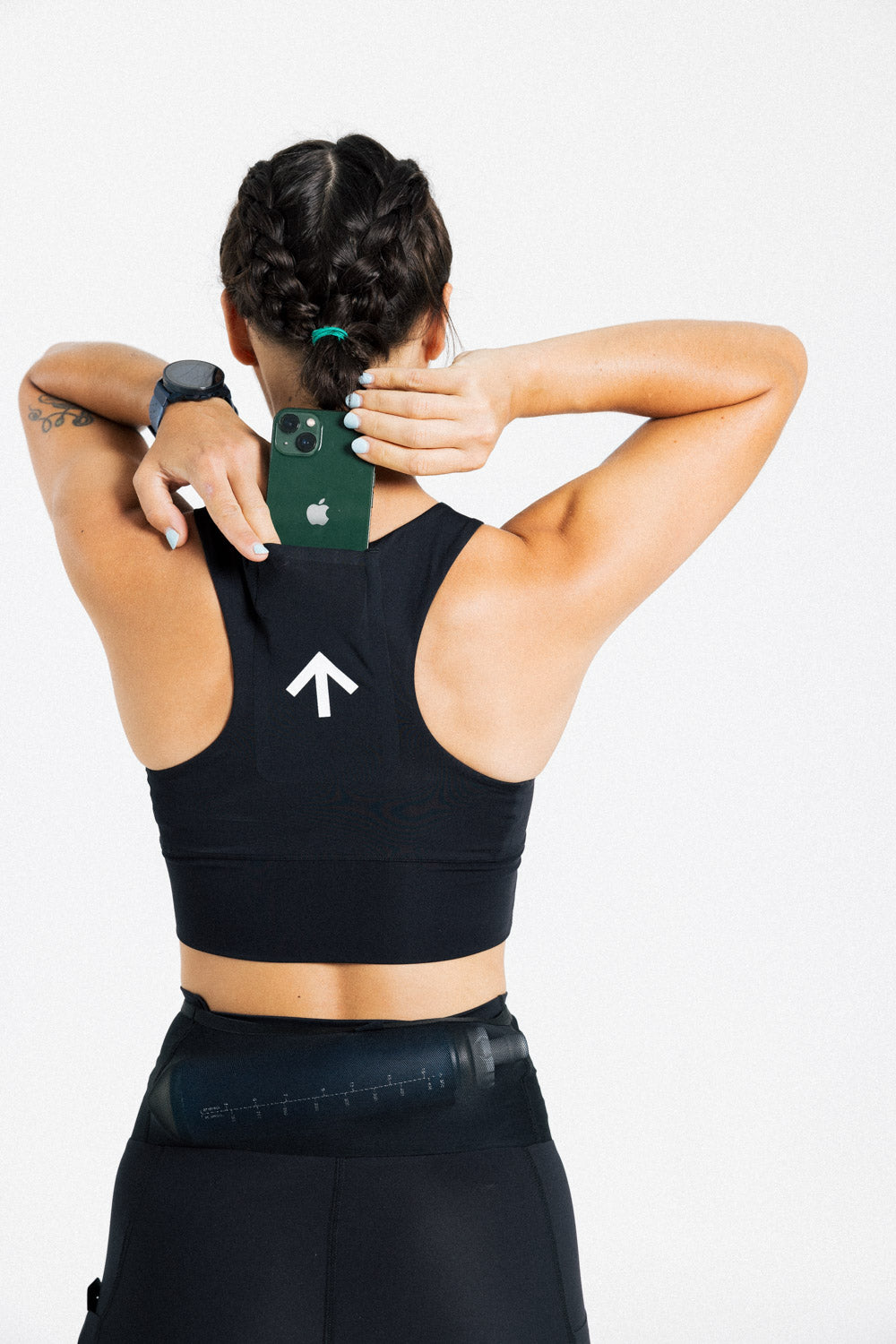 Back view of a female runner storing a phone in the rear pocket of the AROW Women's Running Bra