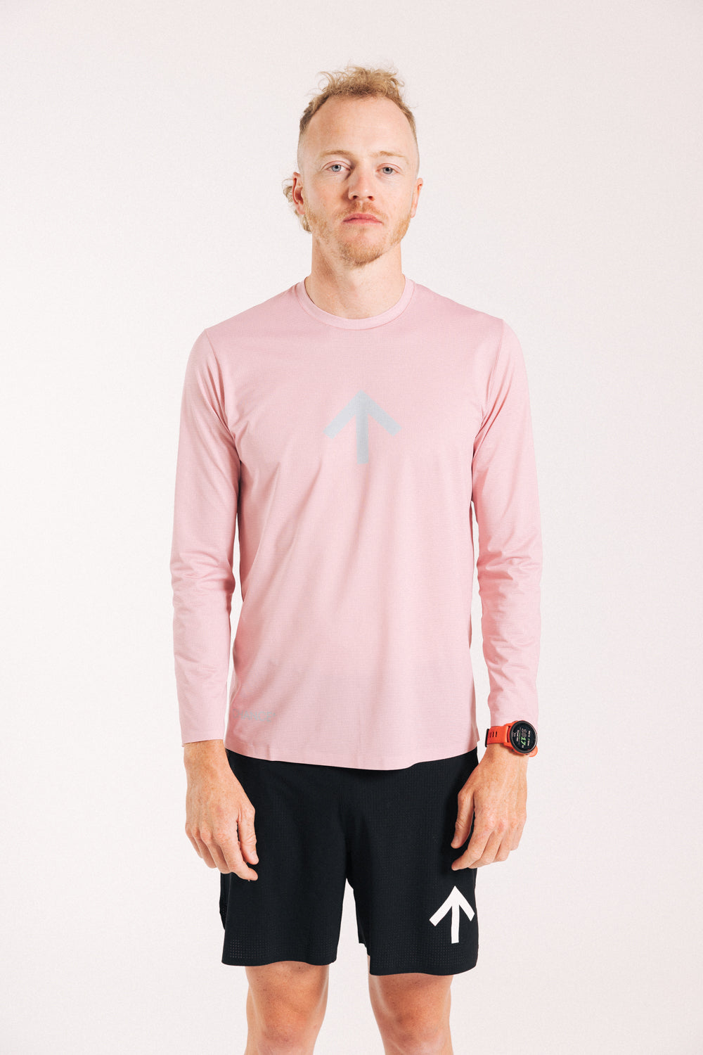 An ultra runner wearing a pink long sleeve running tee with a chrome version of the Chance Running arrow mark on the front.