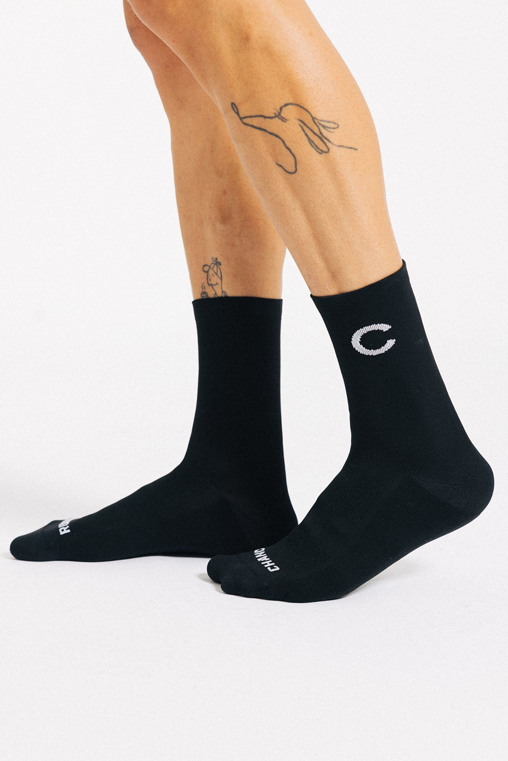 A pair of black and white padded trail running ocks with a geometric pattern, featuring a prominent white arrow and the letter 'C' on the side.