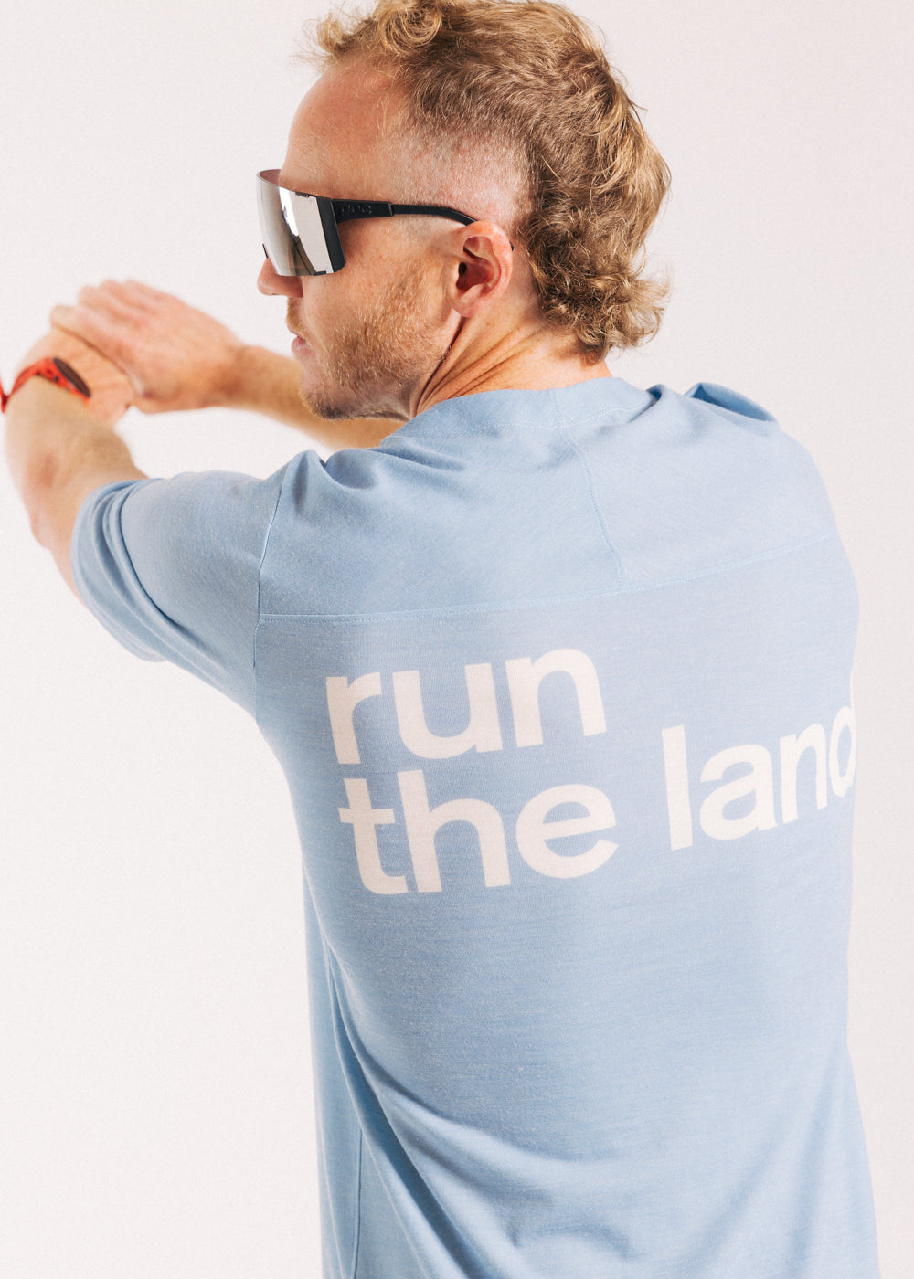 An ultra runner is facing away from the camera wearing a blue merino ultra running tee with the words “run the land” in white on the back.