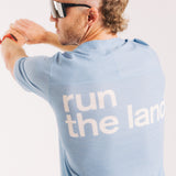 An ultra runner is facing away from the camera wearing a blue merino ultra running tee with the words “run the land” in white on the back.