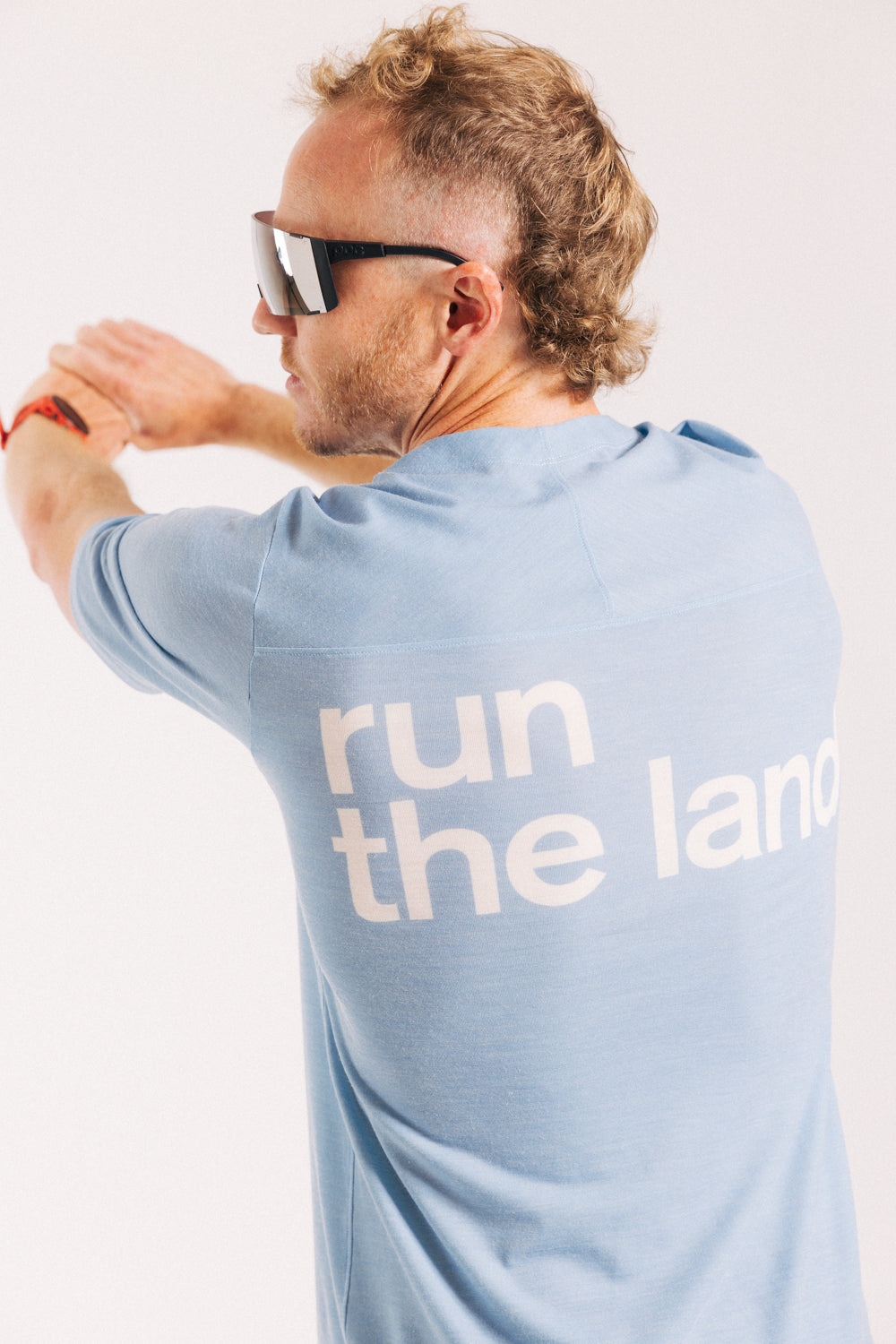 An ultra runner is facing away from the camera wearing a blue merino ultra running tee with the words “run the land” in white on the back.